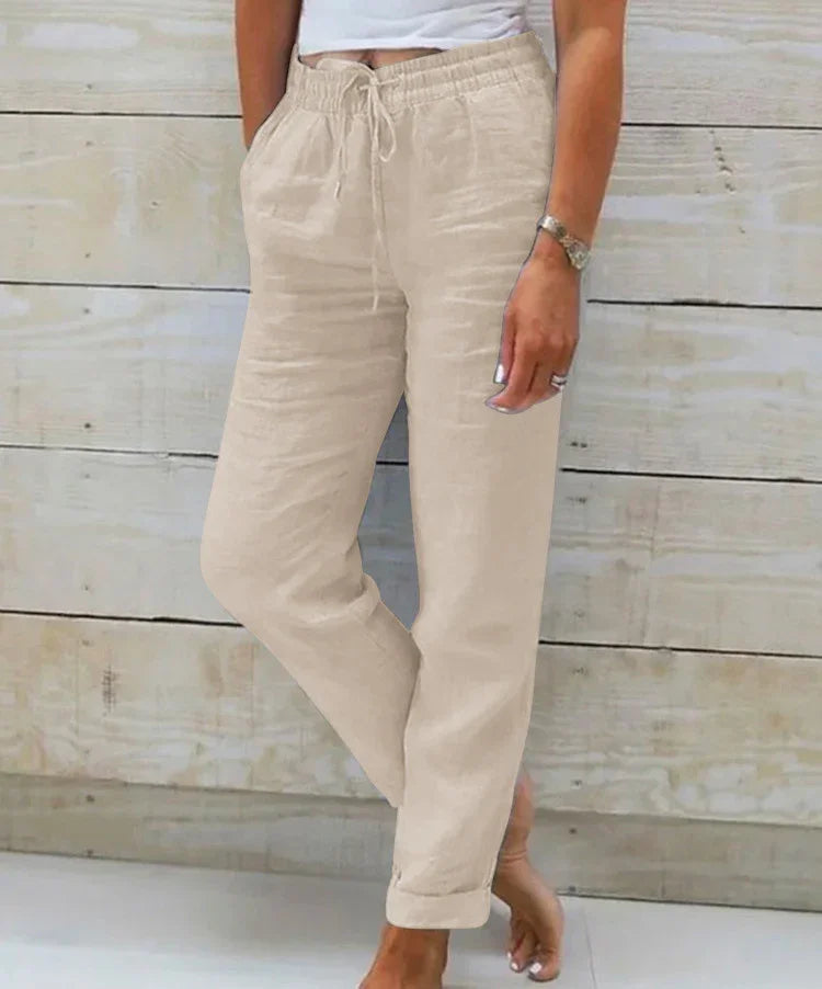 Woman wearing beige linen drawstring casual pants standing barefoot against wooden wall