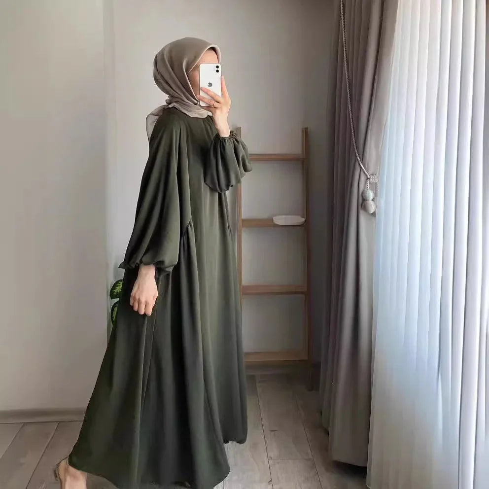Woman wearing olive green modest abaya dress and beige hijab taking mirror selfie indoors
