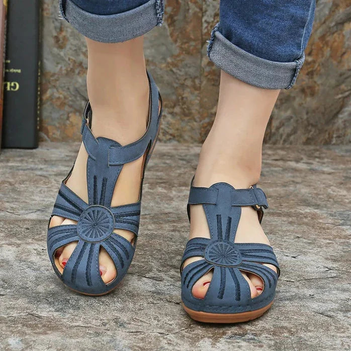 Women's blue leather open-toe sandals with circular design and adjustable straps on stone pavement