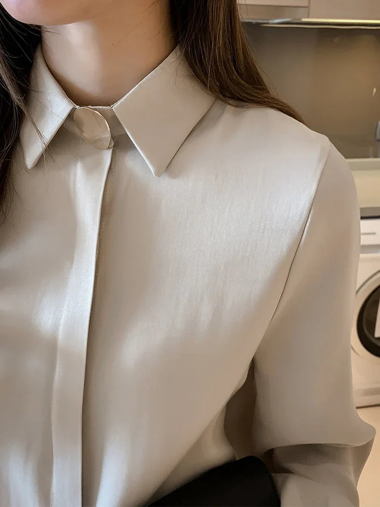 Close-up of woman wearing a beige silky button-up shirt with a classic collar in a modern indoor setting