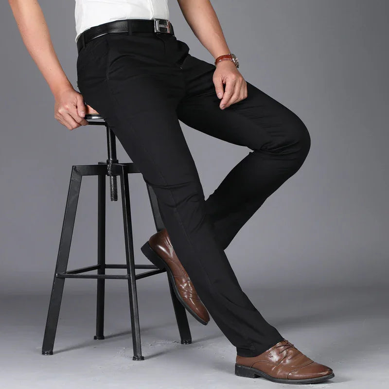 Man wearing slim fit black dress pants, brown leather shoes, and a white shirt sitting on black metal stool
