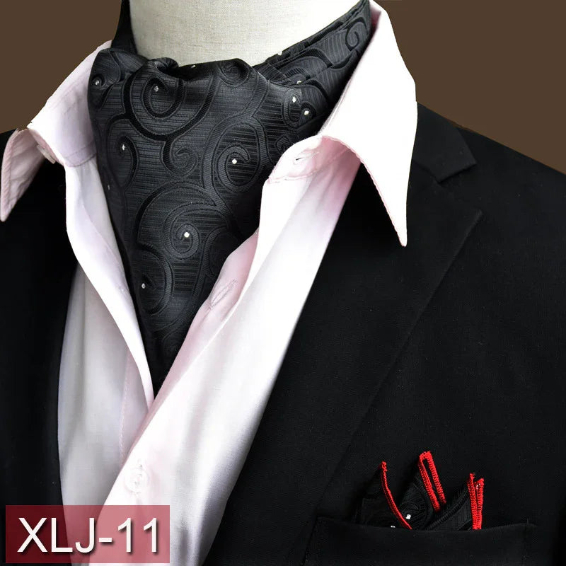 Black paisley patterned ascot tie with white dots paired with a white dress shirt and black suit jacket, red-trimmed pocket square