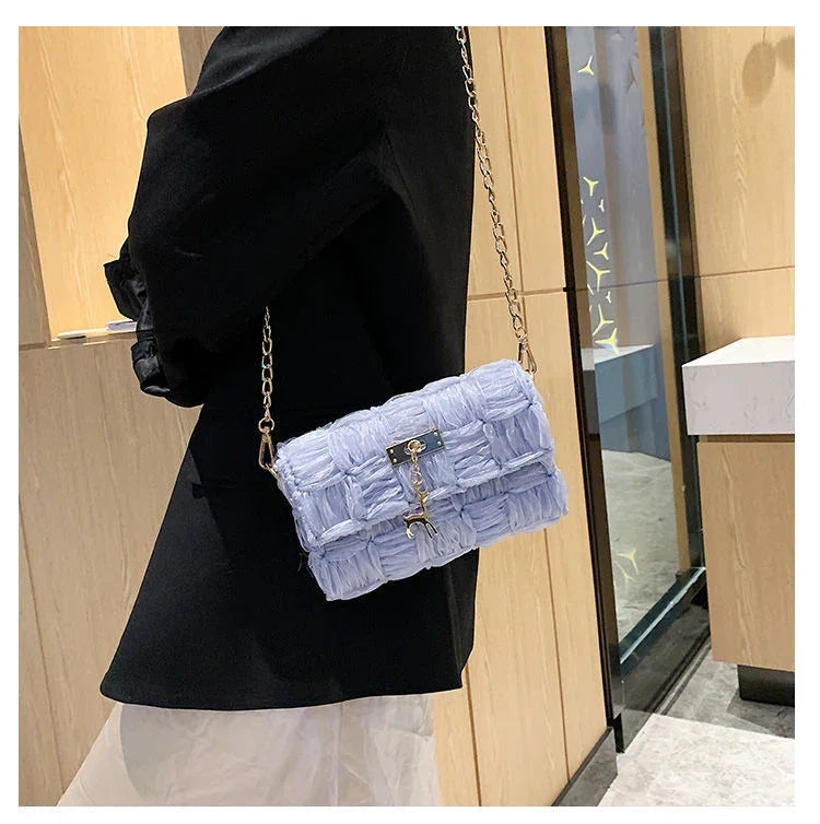 Stylish light purple woven handbag with gold chain strap worn with black blazer indoors