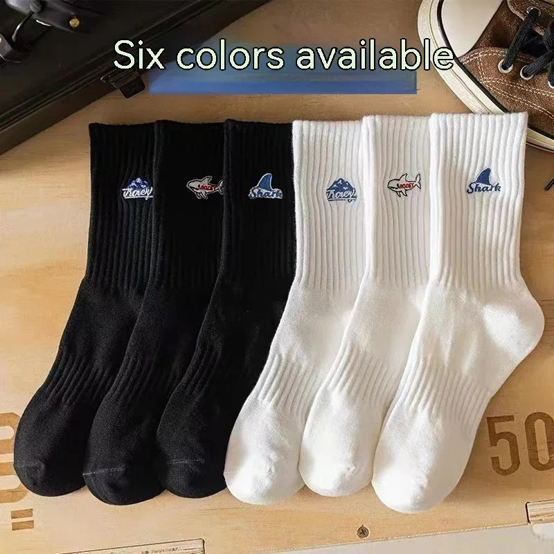 Six black and white crew socks with shark and wave embroidery displayed on wooden surface