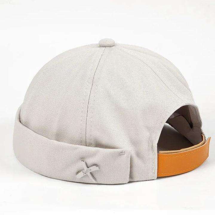 Light beige cotton beanie cap with rolled brim and orange adjustable strap on white background