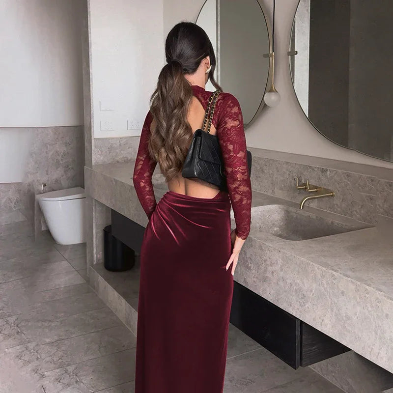 Woman in burgundy velvet and lace open-back dress with black chain handbag in modern bathroom