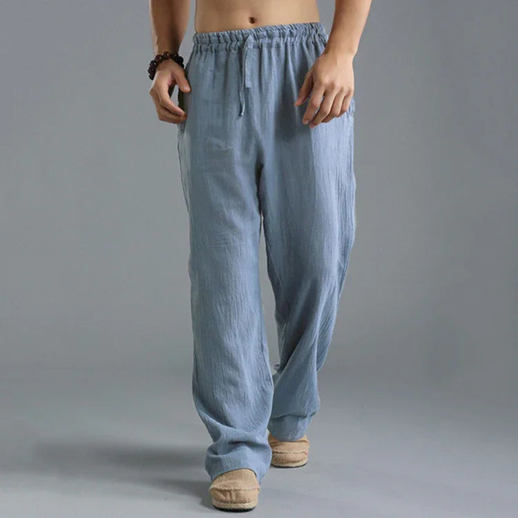 Man wearing light blue casual cotton pants with drawstring and beige slip-on shoes on grey background