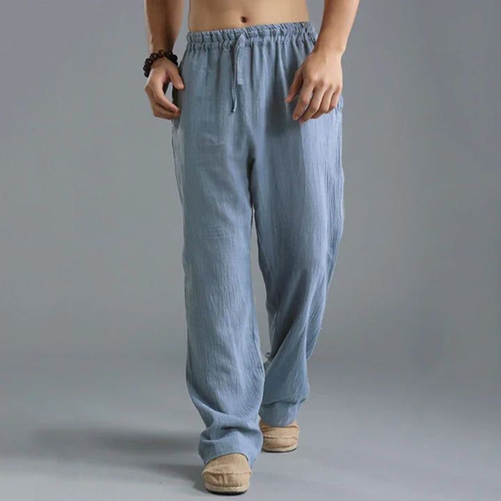 Man wearing light blue casual cotton pants with drawstring and beige slip-on shoes on grey background
