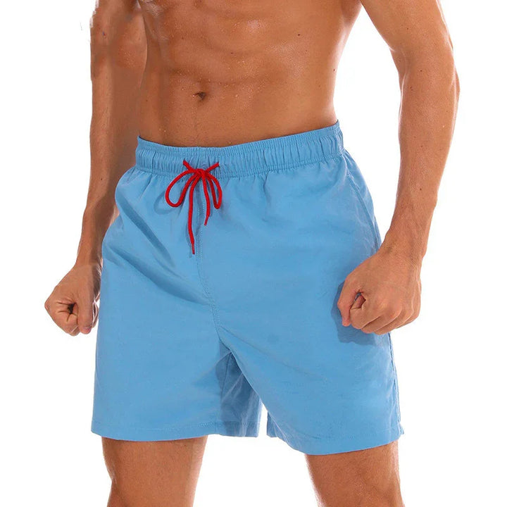 Athletic man wearing light blue swim shorts with red drawstring against white background