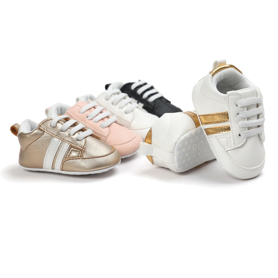 Four pairs of stylish baby sneakers in white, black, pink, and metallic gold with stripes