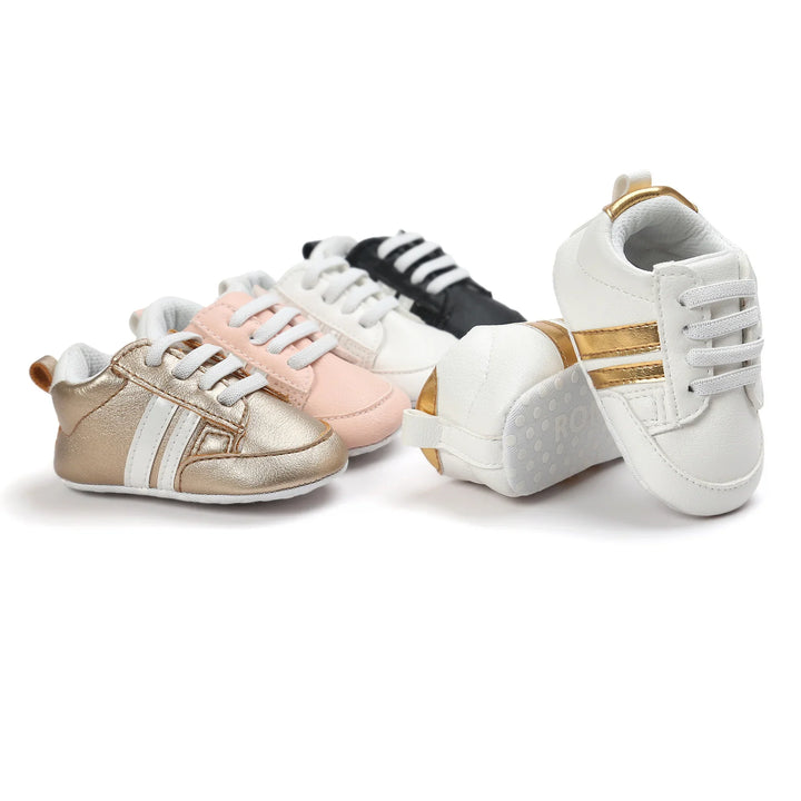 Four pairs of stylish baby sneakers in white, black, pink, and metallic gold with stripes