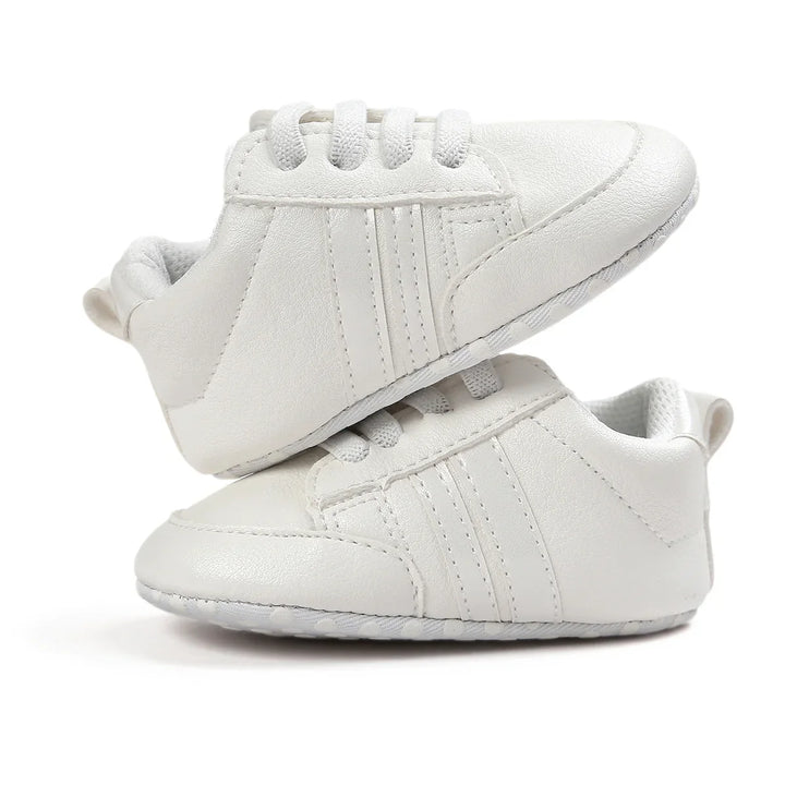 Pair of white baby sneakers with textured soles and laces on white background