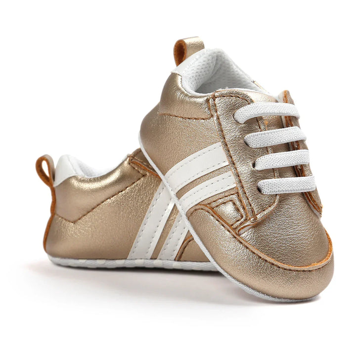 Metallic gold baby sneakers with white stripes and laces on a white background