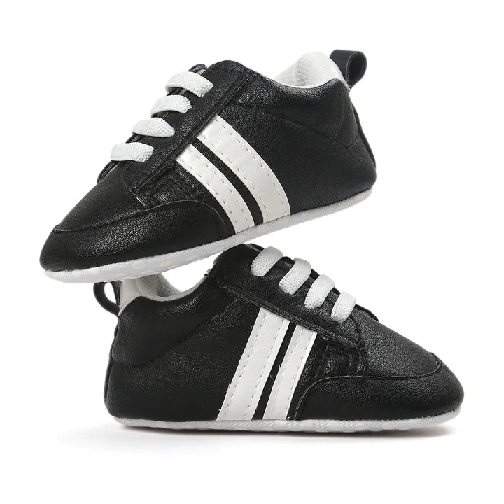 Black baby sneakers with white laces and two white stripes on the sides