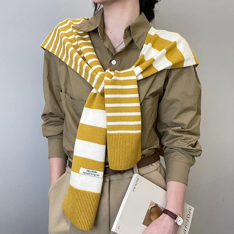 Person wearing olive green shirt and beige pants with mustard yellow and white striped knit scarf draped over shoulders