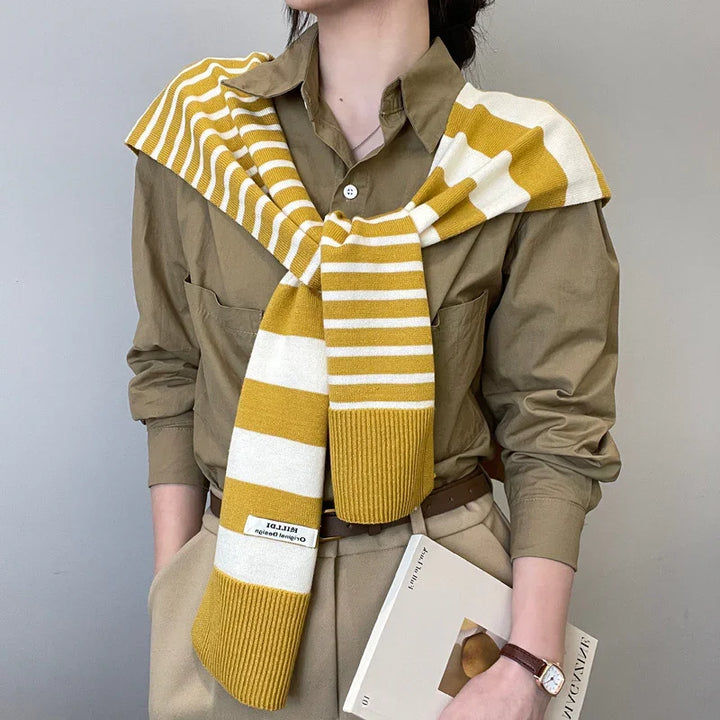 Person wearing olive green shirt and beige pants with mustard yellow and white striped knit scarf draped over shoulders