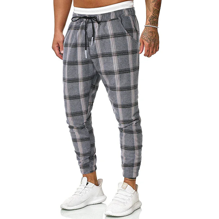 Men's gray plaid jogger pants with drawstring waist and side pockets worn with white sneakers