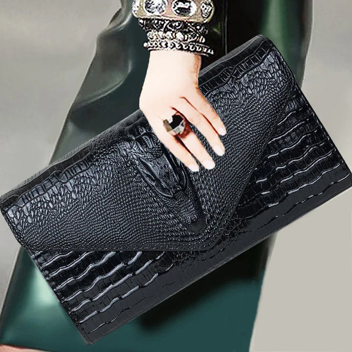 Hand holding black crocodile texture leather clutch bag with ring and studded bracelet