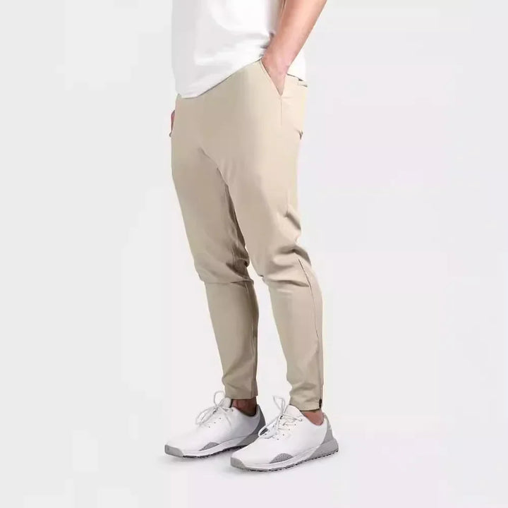Side view of man wearing slim beige jogger pants and white athletic sneakers on white background