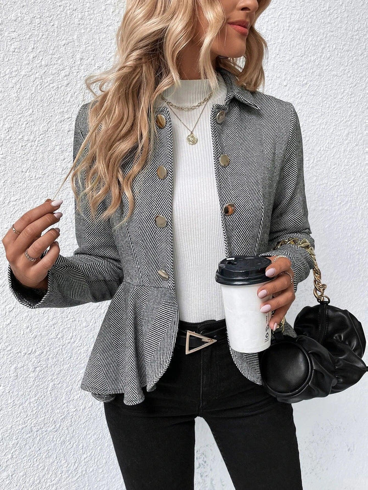 Woman wearing gray herringbone blazer with gold buttons, white turtleneck, black pants, holding coffee cup and black purse