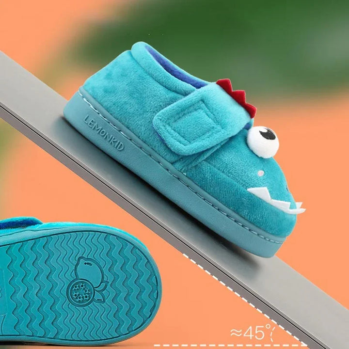 Blue plush kids' slippers with dinosaur design and Velcro strap on angled surface