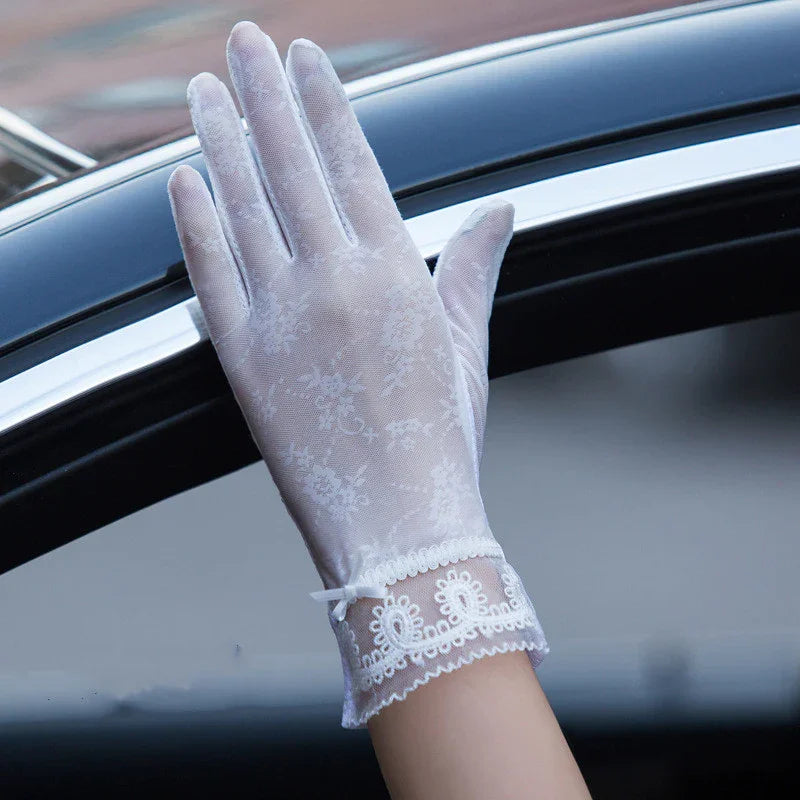 Hand wearing delicate white lace gloves with floral pattern and bow near car window