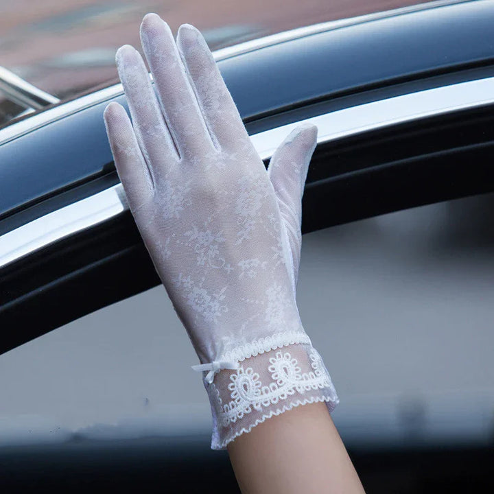 Hand wearing delicate white lace gloves with floral pattern and bow near car window