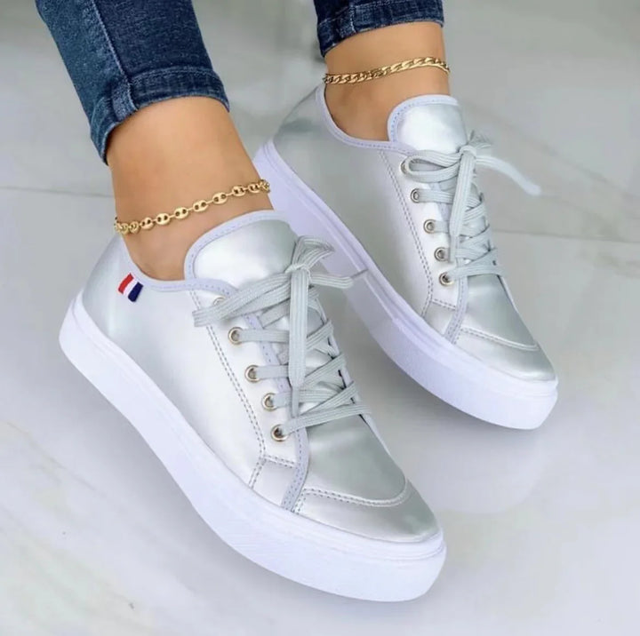 Women wearing silver metallic sneakers with white soles and gold anklets on marble floor