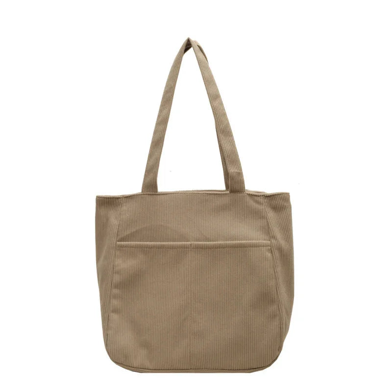 Beige corduroy tote bag with front pocket and two long handles against white background
