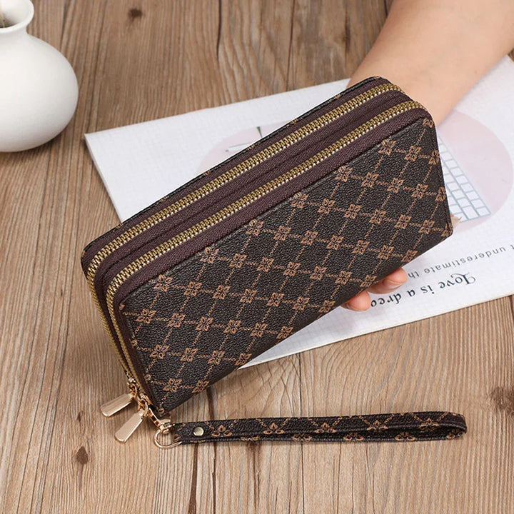 Brown patterned double-zippered wristlet wallet held over wooden table with white vase