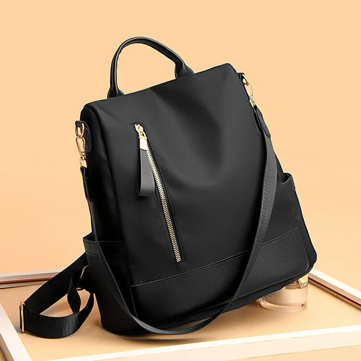 Stylish black backpack with gold zipper detail and adjustable straps on beige background
