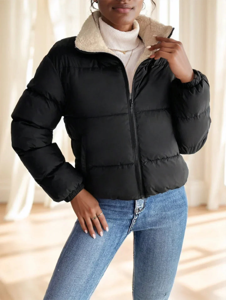 Woman wearing black puffer jacket with sherpa collar and blue jeans in bright indoor setting