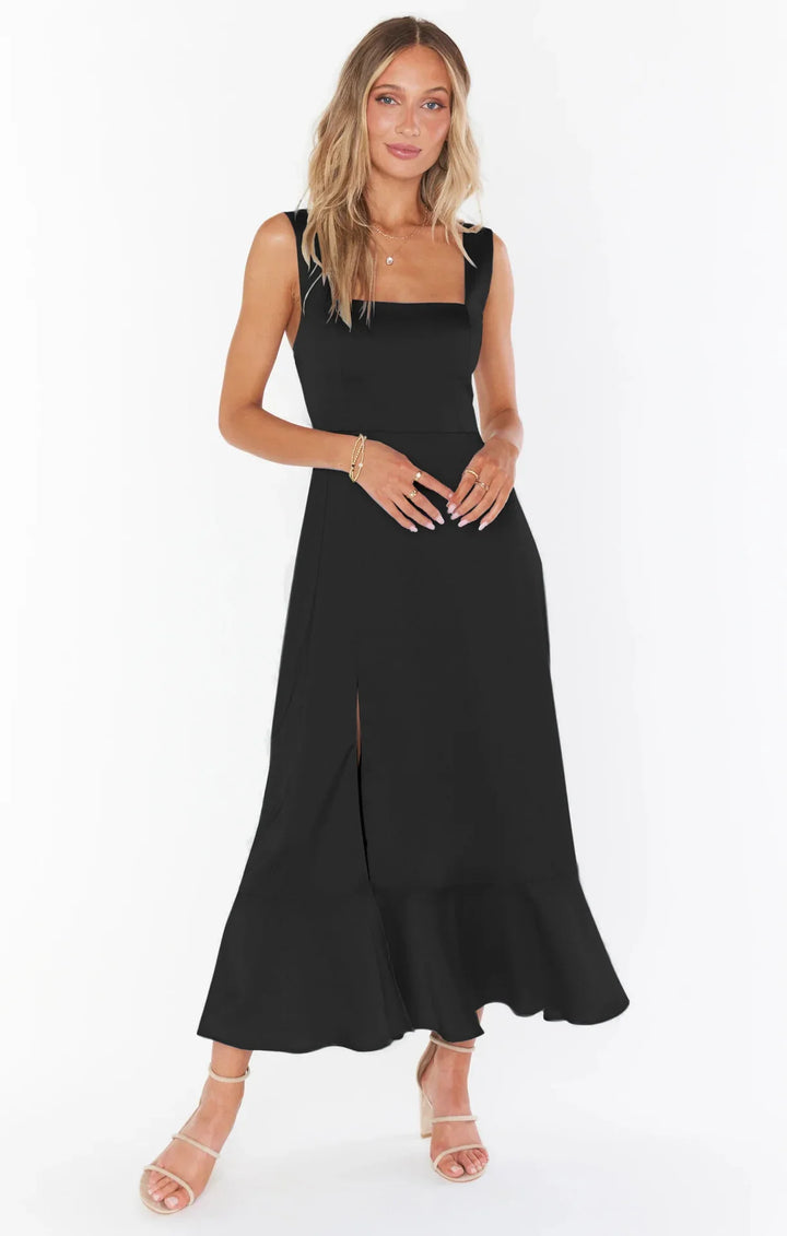 Woman wearing a black sleeveless midi dress with a front slit and ruffled hem, styled with beige heels