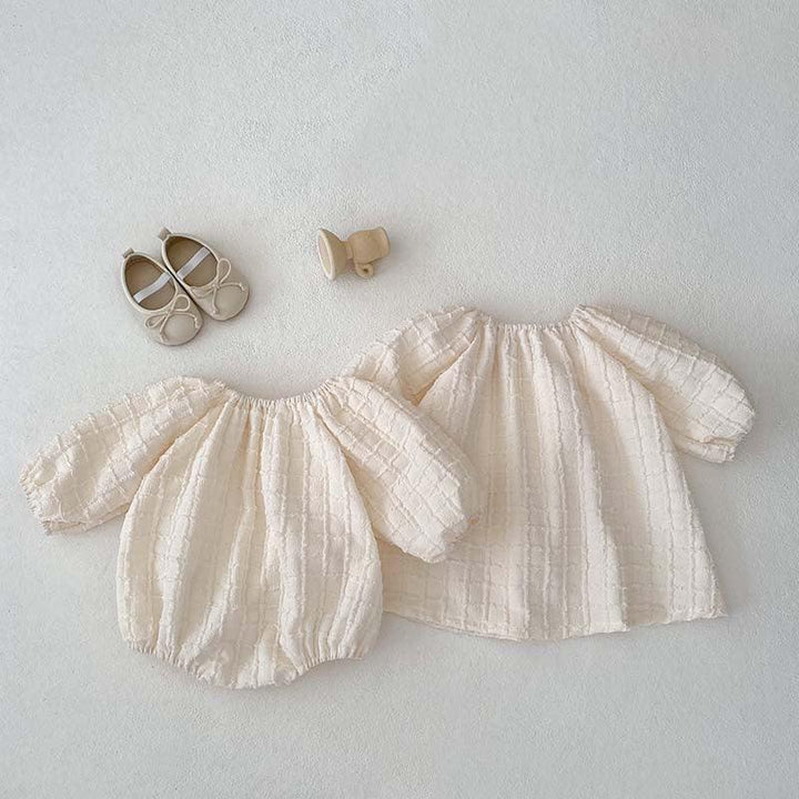 Cream textured baby and toddler matching outfits with beige baby shoes and wooden rattle on white background