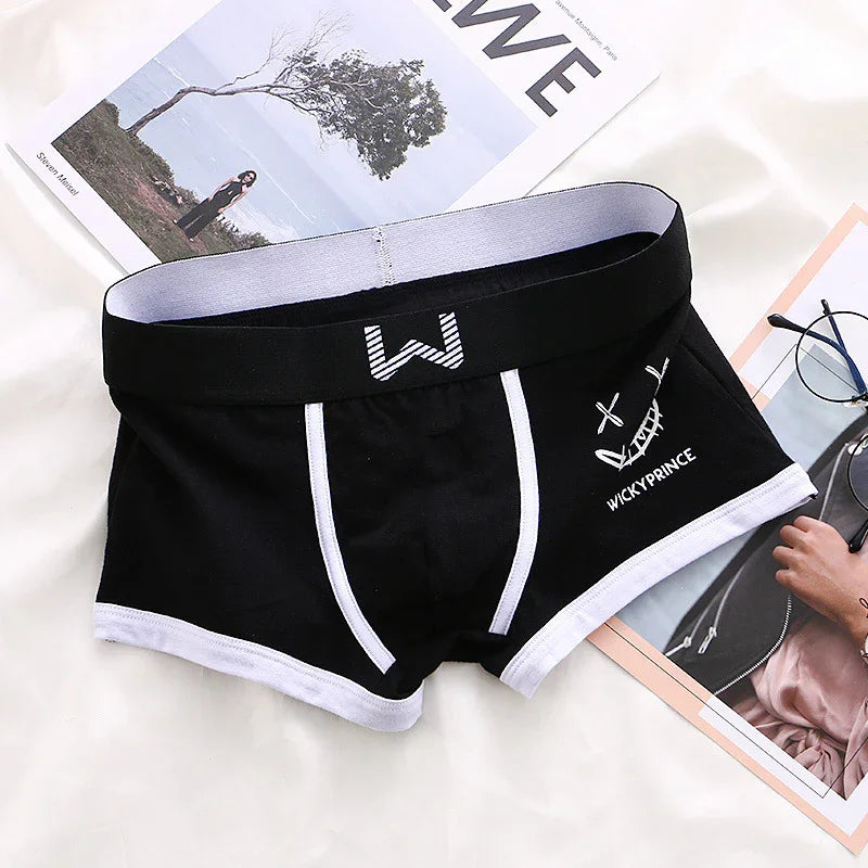 Black men's boxer briefs with white trim and WICKY PRINCE logo, laid on magazines and white fabric
