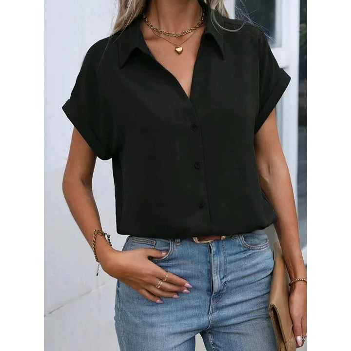 Woman wearing black short-sleeve button-up shirt with gold jewelry and light blue high-waisted jeans