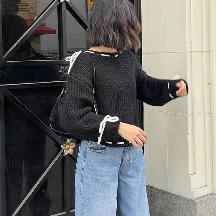 Woman wearing black knit sweater with white lace details and light blue jeans near black door