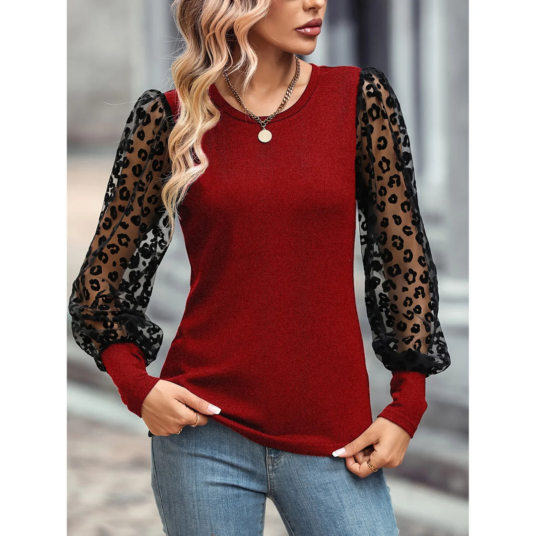 Woman wearing red top with black sheer leopard print puff sleeves and blue jeans