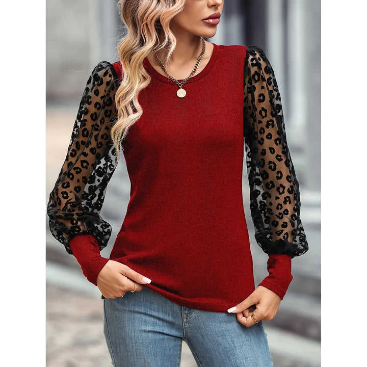 Woman wearing red top with black sheer leopard print puff sleeves and blue jeans