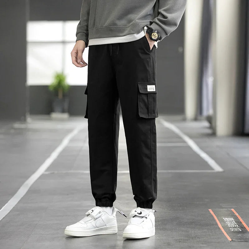 Man wearing black cargo pants with elastic cuffs and white sneakers standing indoors