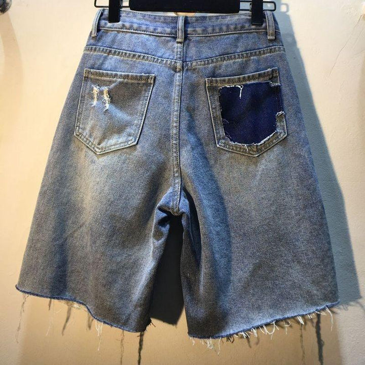 Back view of distressed denim shorts with frayed hem and patched dark blue back pocket hanging on black hanger