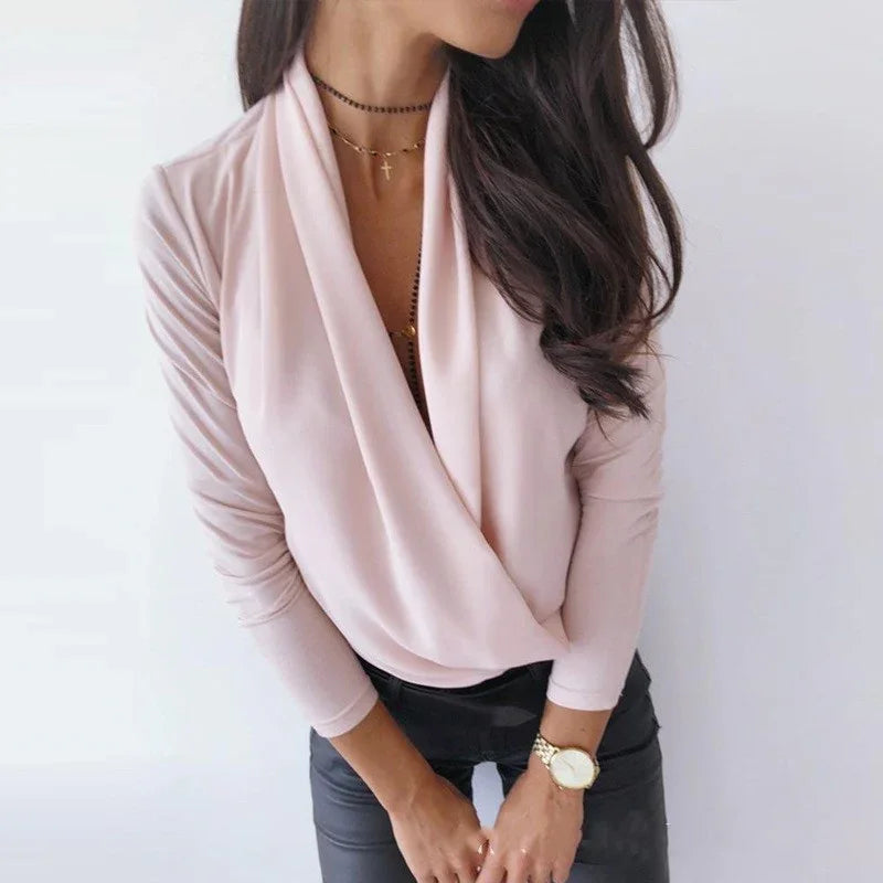 Woman wearing light pink draped blouse with black pants, gold watch, and layered necklaces