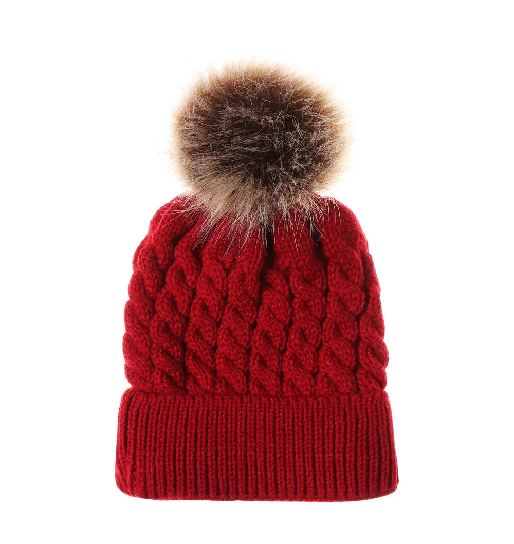 Red knitted winter beanie with cable pattern and large brown faux fur pom pom