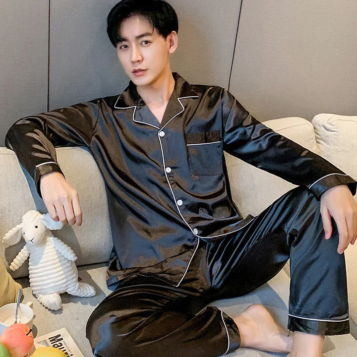 Young man relaxing on sofa wearing black satin pajamas with white piping, holding a stuffed white sheep toy