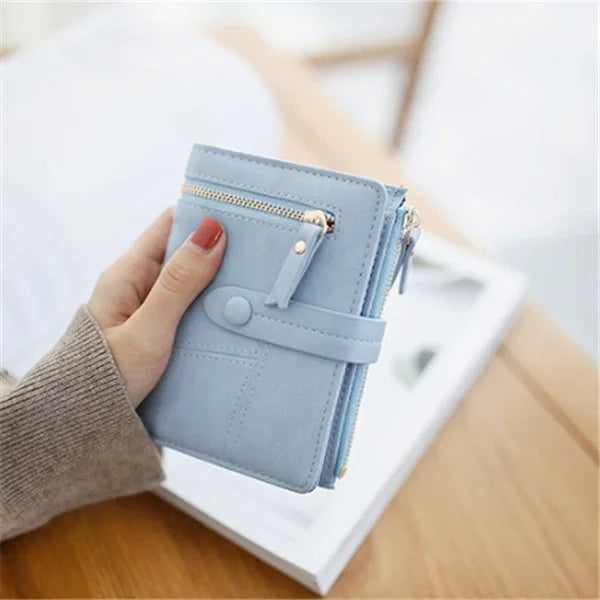 Hand holding a compact light blue wallet with zipper and snap button on a wooden table