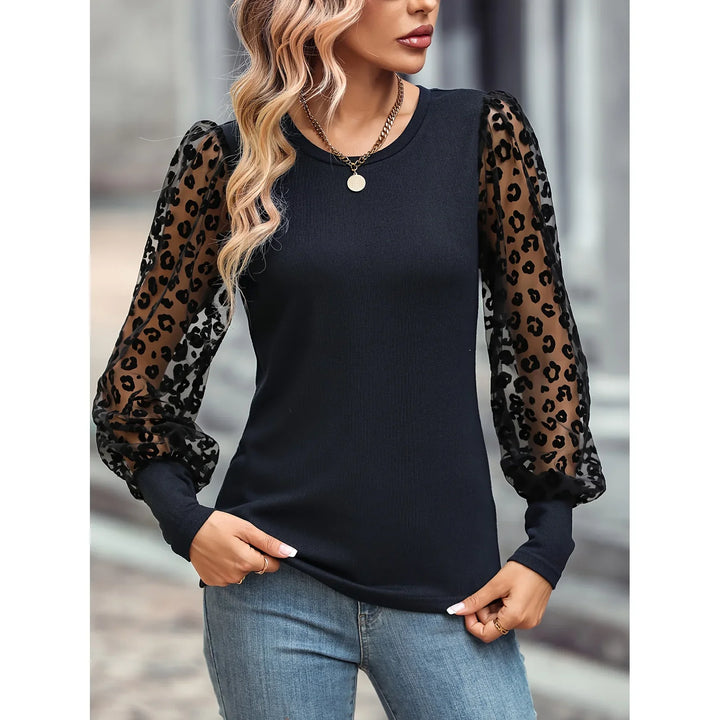 Woman wearing black top with sheer leopard print puff sleeves and gold chain necklace, paired with blue jeans