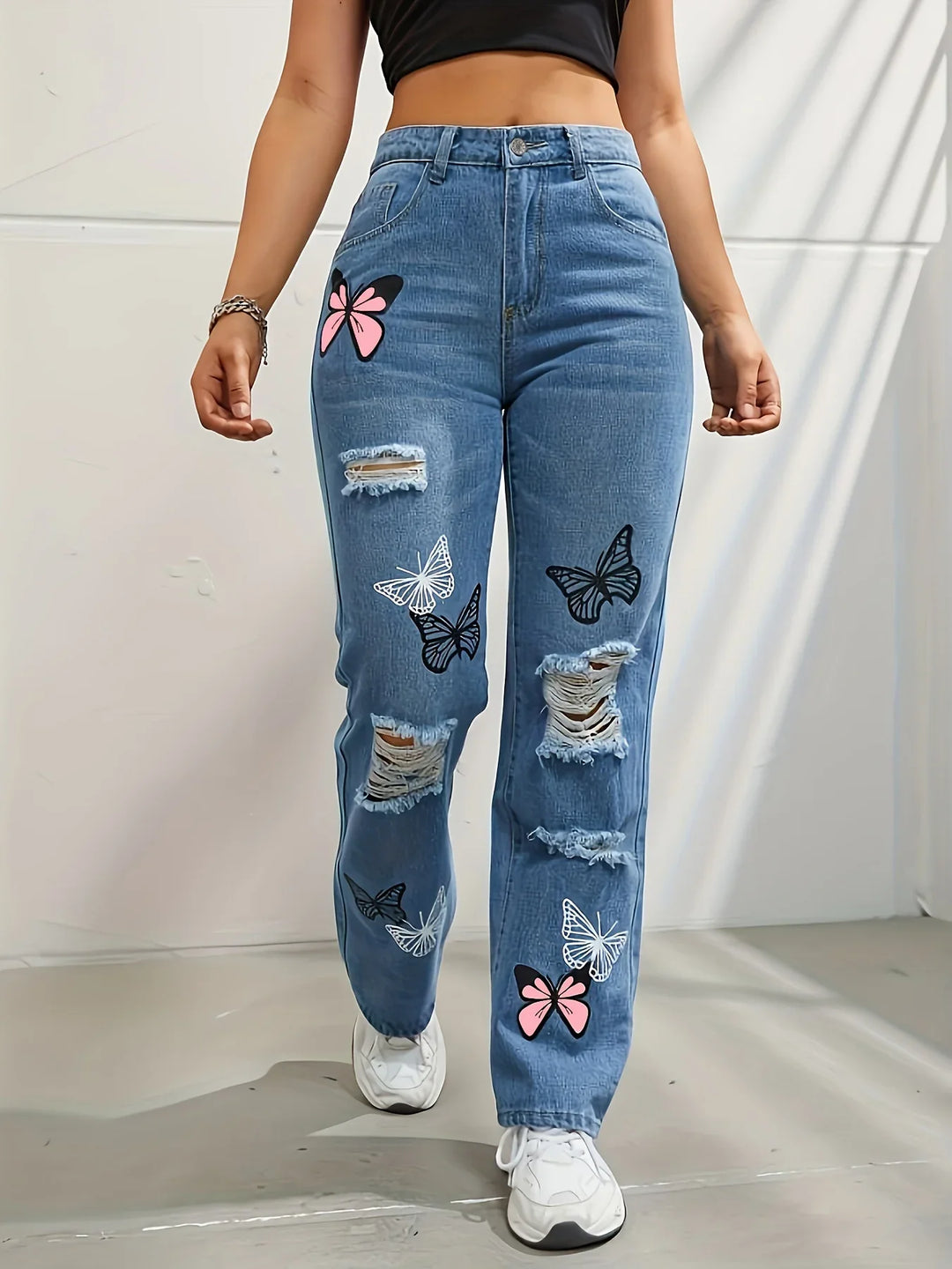 Woman wearing high-waisted blue distressed jeans with butterfly prints and white sneakers