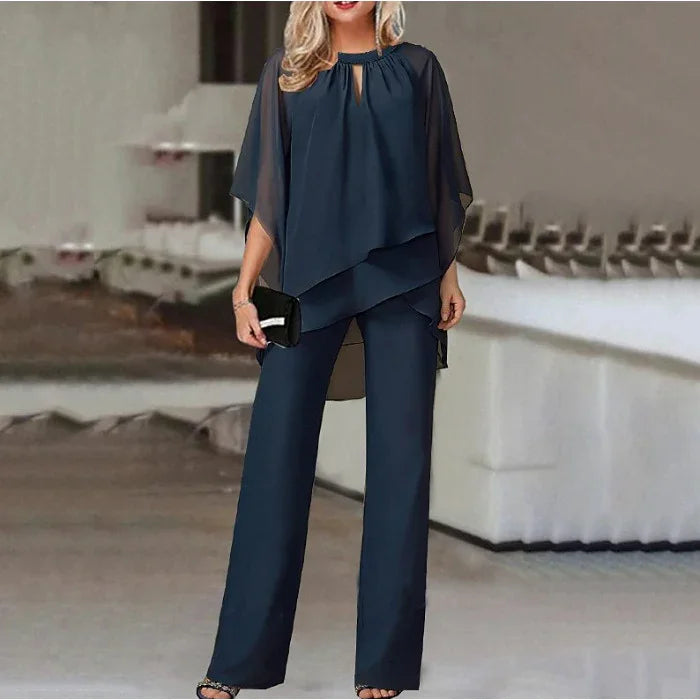 Woman wearing elegant navy chiffon layered blouse and matching wide-leg pants holding black clutch in modern interior
