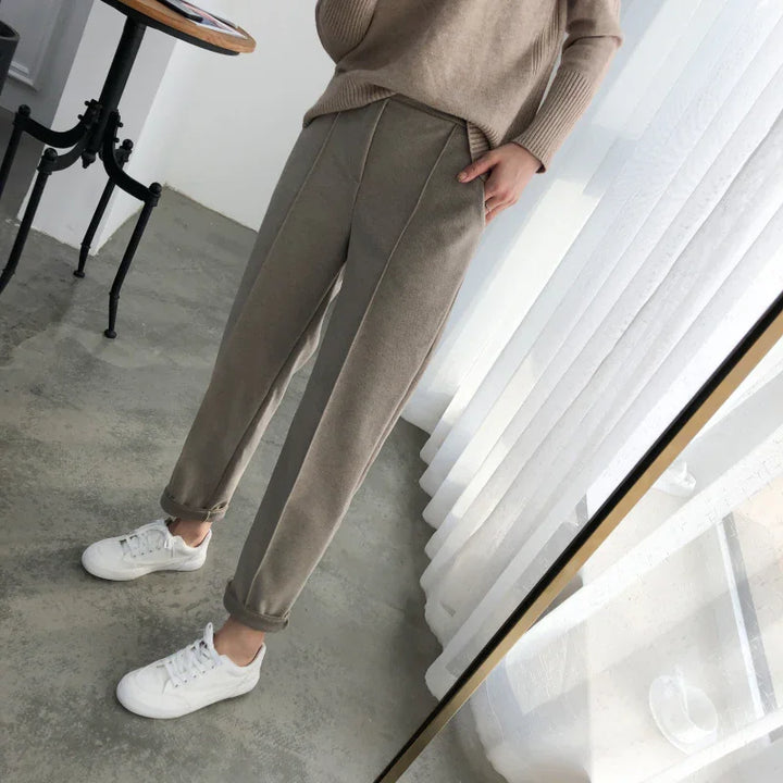 Person wearing beige corduroy pants and white sneakers standing on concrete floor near window with sheer white curtains