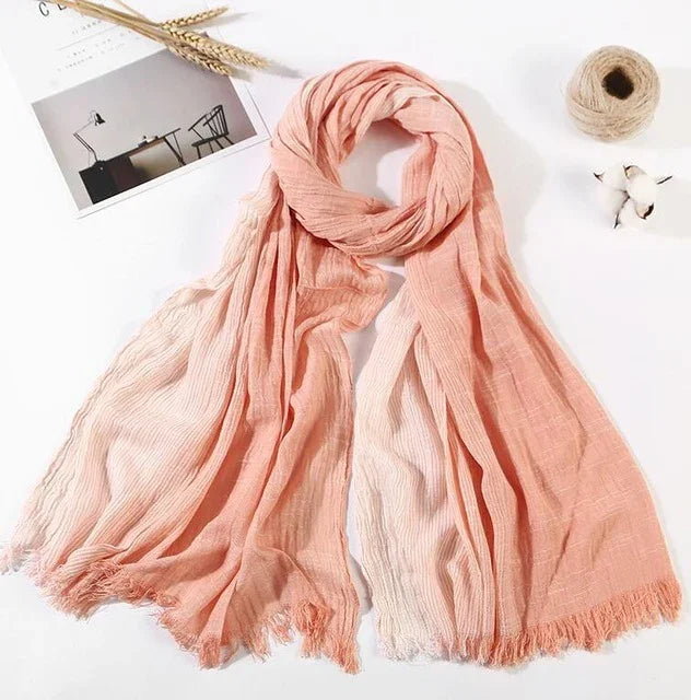 Light pink and peach gradient scarf with fringed edges on white backdrop, styled with wheat, cotton, thread spool
